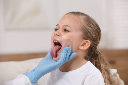 Arzt in Handschuhen untersucht Mundhöhle von Mädchen in Innenräumen