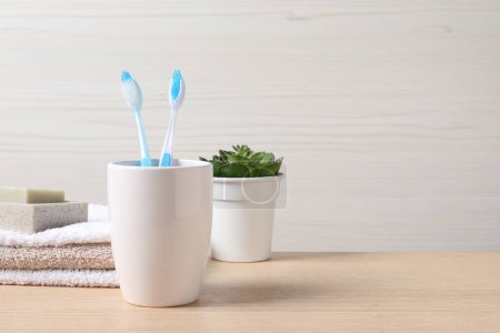 Téléchargez les photos : Brosses à dents en plastique dans le support, savon, serviettes et plante d'intérieur verte sur table en bois, espace pour le texte - en image libre de droit