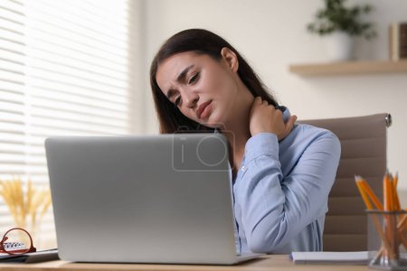 Photo for Young woman suffering from neck pain at table in office - Royalty Free Image
