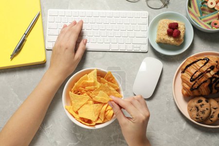Photo for Bad habits. Woman eating different snacks while working on computer at light grey marble table, top view - Royalty Free Image