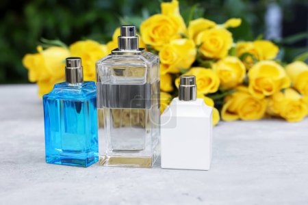 Foto de Perfumes y hermoso ramo de rosas amarillas en mesa de luz al aire libre, enfoque selectivo. Espacio para texto - Imagen libre de derechos