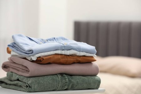Stack of different folded clothes on table indoors, closeup. Space for text