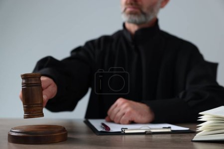 Foto de Juez con mazo y papeles sentados a la mesa de madera sobre fondo gris claro, primer plano - Imagen libre de derechos