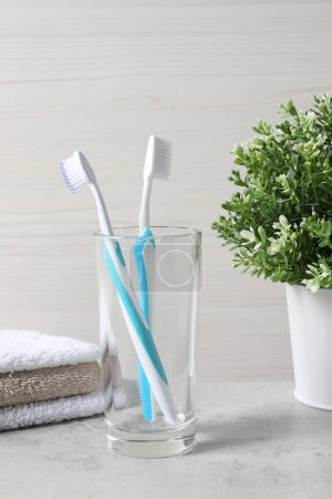 Téléchargez les photos : Brosses à dents en plastique dans un support en verre et serviettes sur table gris clair - en image libre de droit
