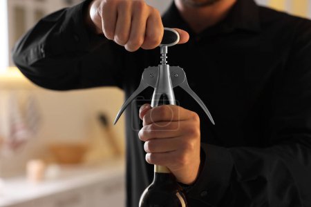 Man opening wine bottle with corkscrew indoors, closeup