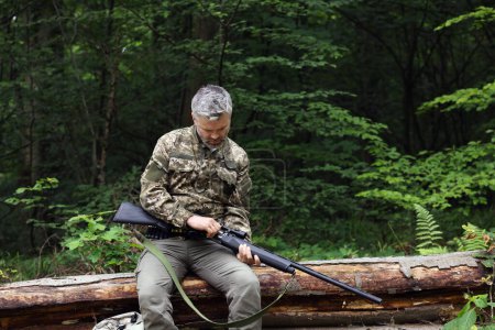 Photo for Man with hunting rifle sitting on fallen tree in forest. Space for text - Royalty Free Image