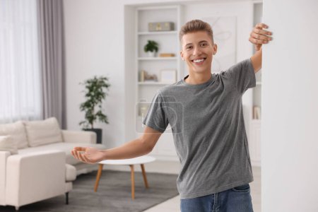 Téléchargez les photos : Homme heureux accueillant près du mur blanc à la maison. Invitation à venir dans la chambre - en image libre de droit