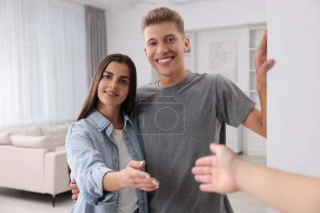 Téléchargez les photos : Heureux couple accueillant leur invité près du mur blanc à la maison. Invitation à venir dans la chambre - en image libre de droit