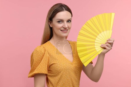 Foto de Mujer feliz con abanico de mano amarillo sobre fondo rosa - Imagen libre de derechos