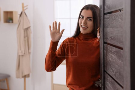 Téléchargez les photos : Femme heureuse agitant près de la porte, espace pour le texte. Invitation à venir à l'intérieur - en image libre de droit
