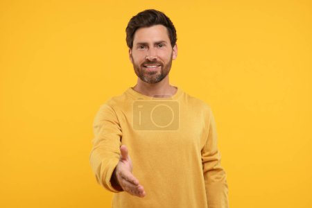 Téléchargez les photos : Homme heureux accueillant et offrant poignée de main sur fond orange - en image libre de droit