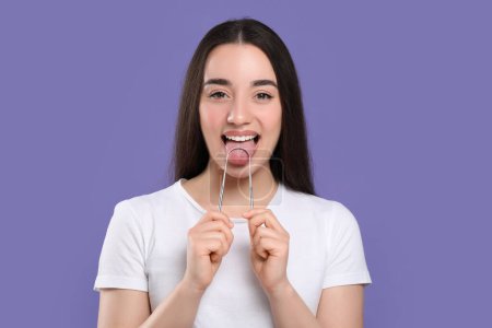 Foto de Mujer feliz cepillándose la lengua con limpiador sobre fondo violeta - Imagen libre de derechos