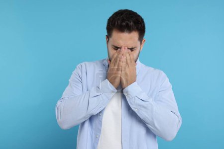 Photo for Resentful man covering face with hands on light blue background - Royalty Free Image