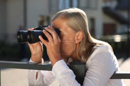 Téléchargez les photos : Concept de vie privée. Femme âgée curieuse avec des jumelles espionnant les voisins au-dessus de la clôture à l'extérieur - en image libre de droit