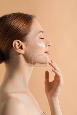 Photo for Beautiful young woman with sun protection cream on her face against beige background - Royalty Free Image
