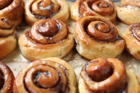 Tasty cinnamon rolls with cream on parchment paper, closeup
