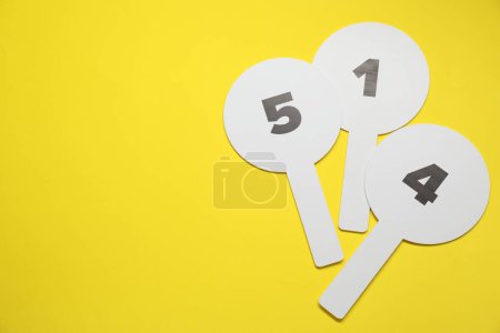 Photo for Auction paddles with numbers on yellow background, flat lay. Space for text - Royalty Free Image