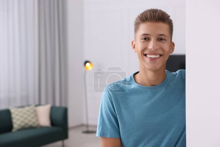 Téléchargez les photos : Homme heureux debout près du mur blanc à la maison, espace pour le texte. Invitation à venir dans la chambre - en image libre de droit