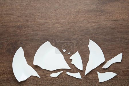 Photo for Pieces of broken ceramic plate on wooden table, flat lay. Space for text - Royalty Free Image