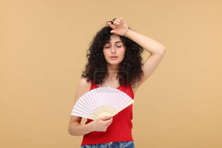 Foto de Mujer con abanico de mano sufriendo de calor sobre fondo beige - Imagen libre de derechos