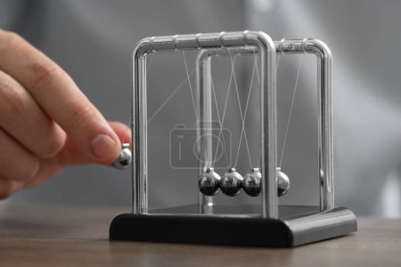 Photo for Man playing with Newton's cradle at table, closeup. Physics law of energy conservation - Royalty Free Image