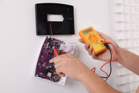 Foto de Hombre usando multímetro digital durante la instalación del sistema de alarma de seguridad del hogar en la pared blanca en el interior, primer plano - Imagen libre de derechos