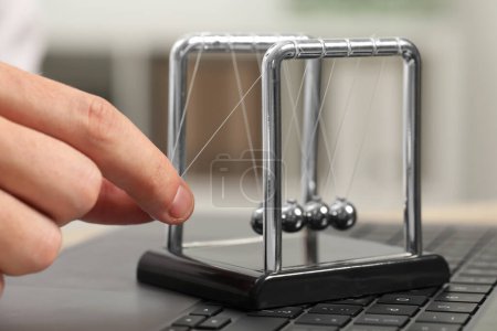Photo for Man playing with Newton's cradle on laptop keyboard, closeup. Physics law of energy conservation - Royalty Free Image