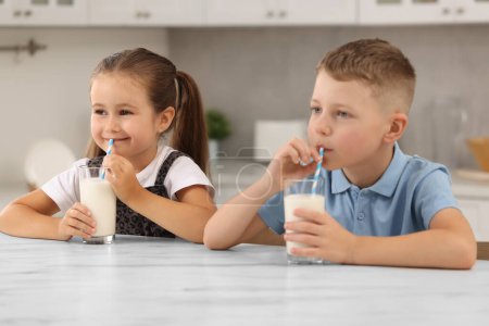 Téléchargez les photos : Enfants mignons boire du lait frais à partir de verres à table blanche dans la cuisine - en image libre de droit