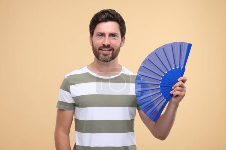 Foto de Hombre feliz sosteniendo ventilador de mano sobre fondo beige - Imagen libre de derechos