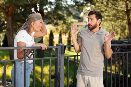 Foto de Vecinos emocionales discutiendo cerca de la valla al aire libre - Imagen libre de derechos