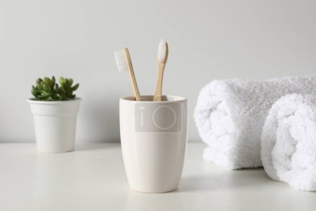 Téléchargez les photos : Brosses à dents en bambou dans le support, plante en pot et serviettes sur comptoir blanc - en image libre de droit