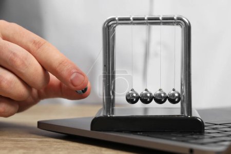 Photo for Man playing with Newton's cradle and laptop on wooden table, closeup. Physics law of energy conservation - Royalty Free Image
