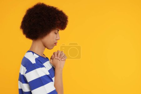 Mujer con las manos cerradas rezando a Dios sobre fondo naranja. Espacio para texto