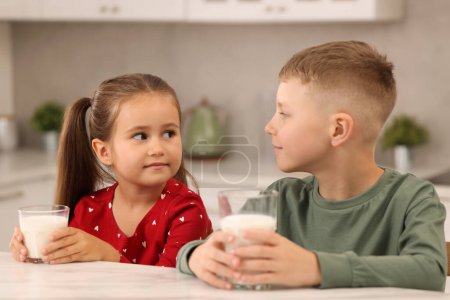 Téléchargez les photos : Enfants mignons avec des verres de lait à la table blanche dans la cuisine - en image libre de droit