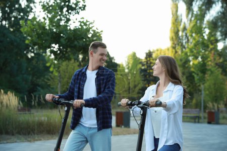 Photo for Happy couple riding modern electric kick scooters in park - Royalty Free Image