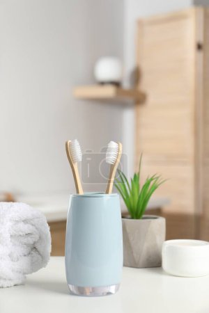 Téléchargez les photos : Brosses à dents en bambou, serviette, plantes en pot et produits cosmétiques sur comptoir blanc dans la salle de bain - en image libre de droit