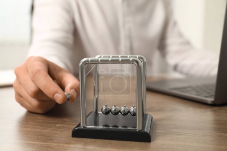 Photo for Man playing with Newton's cradle at office table, closeup. Physics law of energy conservation - Royalty Free Image