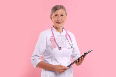 Téléchargez les photos : Docteur avec ruban rose, presse-papiers et stéthoscope sur fond de couleur. Sensibilisation au cancer du sein - en image libre de droit