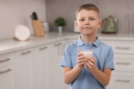 Téléchargez les photos : Garçon mignon avec verre de lait frais dans la cuisine, espace pour le texte - en image libre de droit