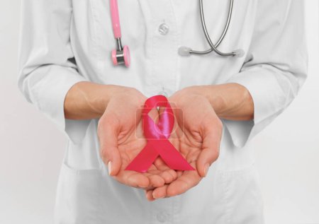 Téléchargez les photos : Docteur avec stéthoscope tenant un ruban rose sur fond blanc, gros plan. Sensibilisation au cancer du sein - en image libre de droit