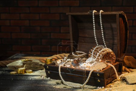 Chest with treasures and scattered sand on wooden floor, space for text