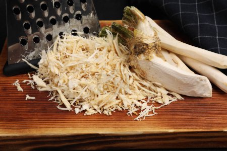 Photo for Board with grated horseradish, peeled roots and grater on black background, closeup - Royalty Free Image