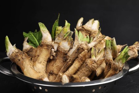 Photo for Fresh horseradish roots in metal colander on black background, closeup - Royalty Free Image