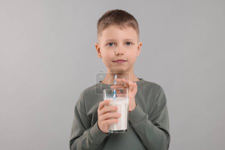 Téléchargez les photos : Mignon garçon avec verre de lait frais sur fond gris clair - en image libre de droit