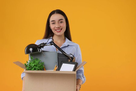 Téléchargez les photos : Heureuse femme au chômage tenant boîte avec effets personnels de bureau sur fond orange, espace pour le texte - en image libre de droit