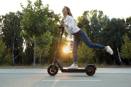 Photo for Happy woman riding modern electric kick scooter in park - Royalty Free Image