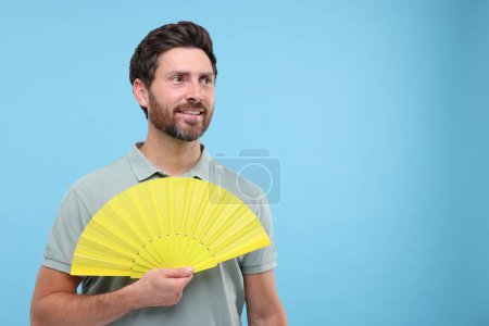 Foto de Hombre feliz sosteniendo ventilador de mano sobre fondo azul claro. Espacio para texto - Imagen libre de derechos
