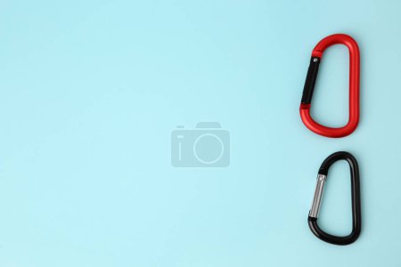 Photo for Two metal carabiners on light blue background, flat lay. Space for text - Royalty Free Image
