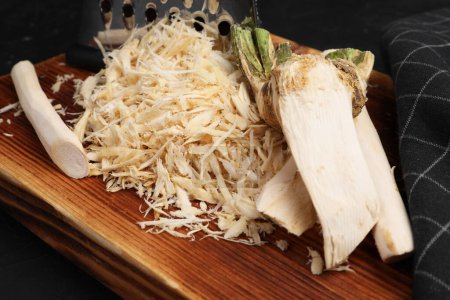 Photo for Board with grated horseradish and peeled roots on black table, closeup - Royalty Free Image