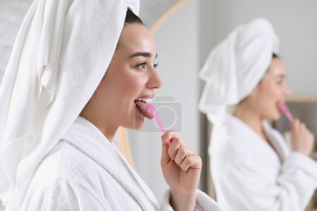 Happy woman brushing her tongue with cleaner in bathroom, space for text